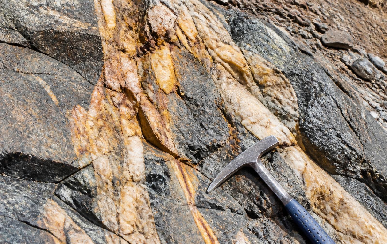 Afloramento mineralizado com veios oxidados e martelo geológico como escala